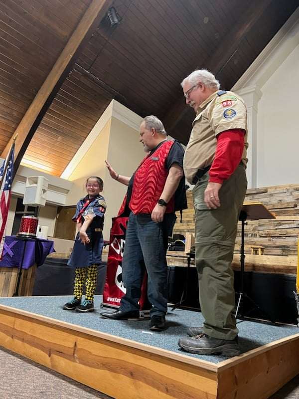 A Cub Scout on stage with Carroll Baker and a pack leader during a Blue and Gold banquet show